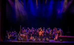 Oliver Rajamani performing with a guitar and ensemble on stage