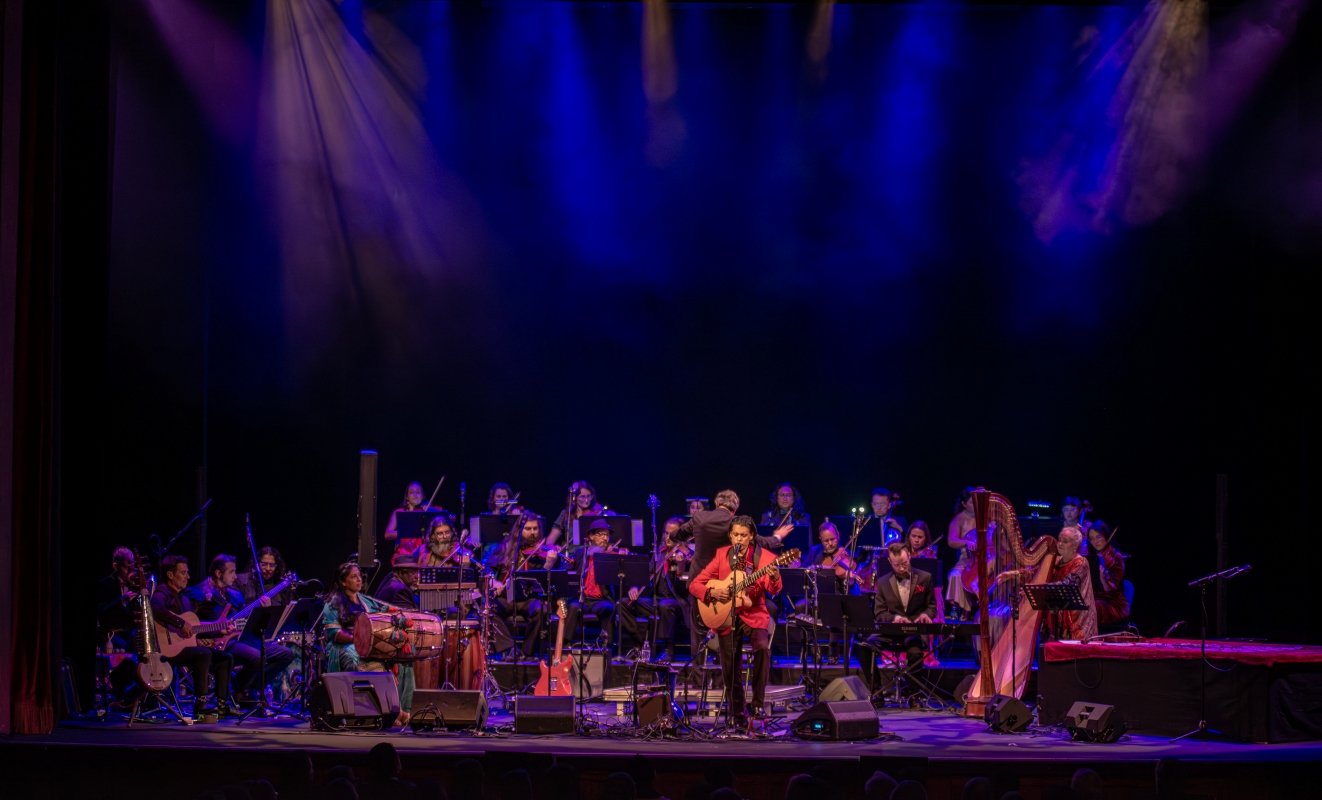 Oliver Rajamani performing with a guitar and ensemble on stage